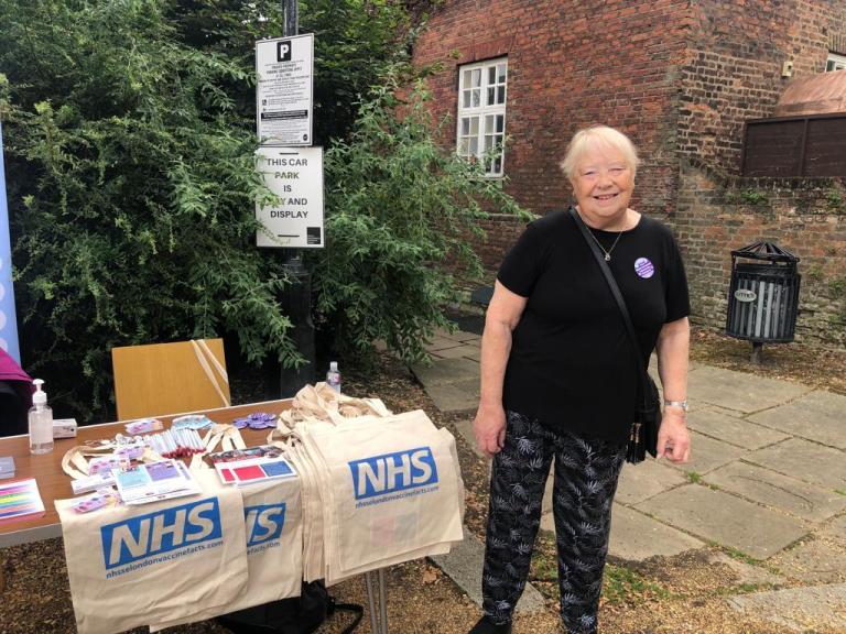 A lady volunteer standing next to a Greenwich Supports table