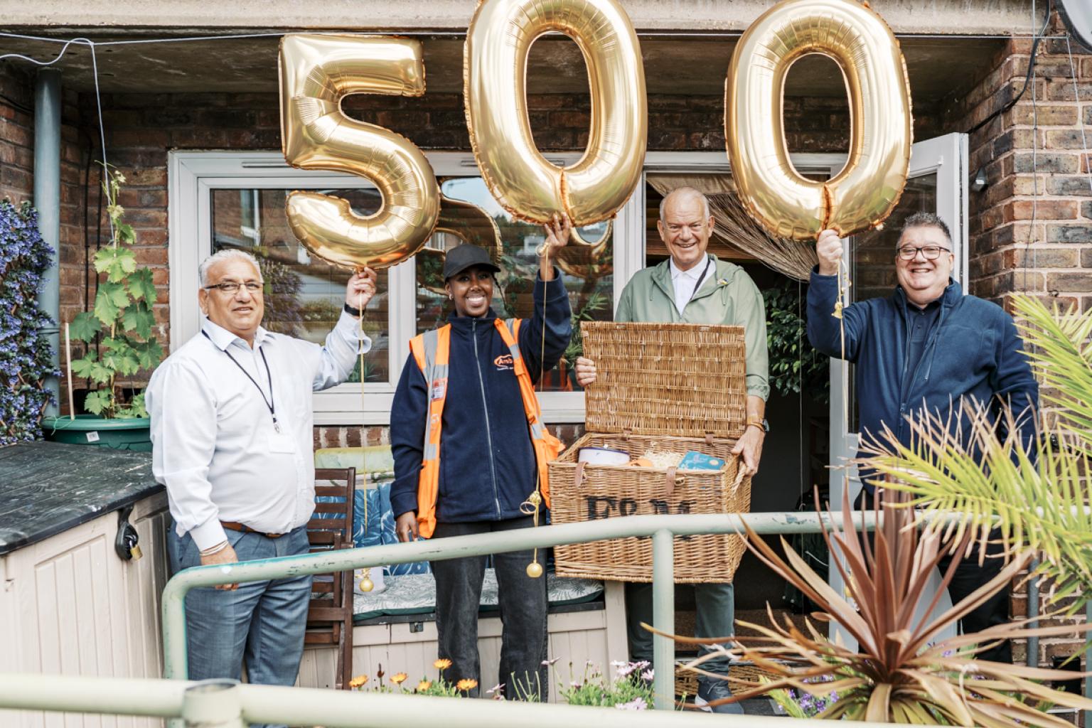People standing in a kitchen with gold balloons displaying 5-0-0