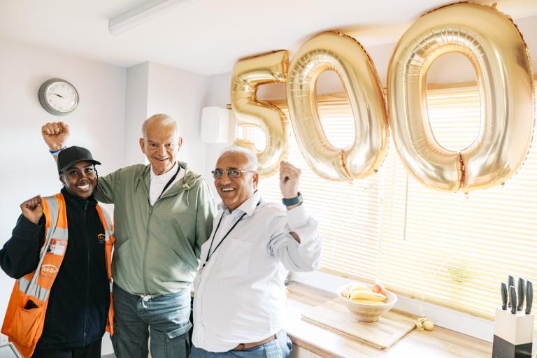 People standing in a kitchen with gold balloons displaying 5-0-0